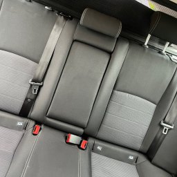 Dorian mroz - Szara tapicerka tylnej kanapy samochodowej z widocznymi pasami bezpieczeństwa i zagłówkami, w neutralnym świetle.