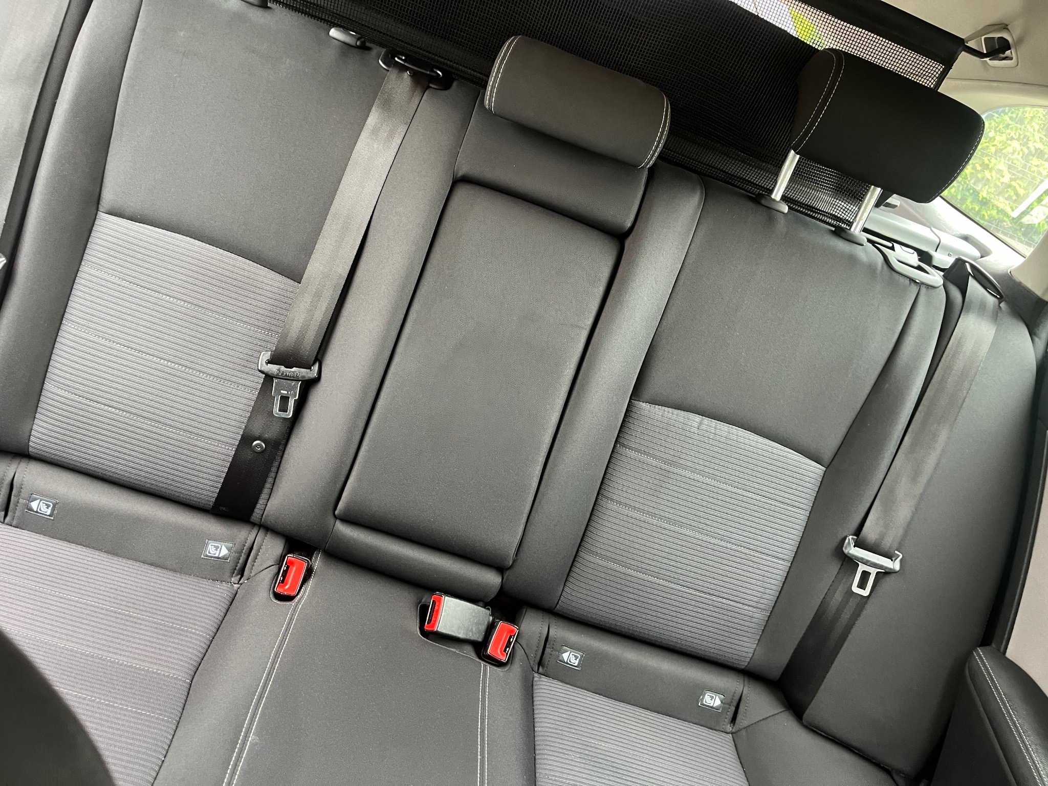 Szara tapicerka tylnej kanapy samochodowej z widocznymi pasami bezpieczeństwa i zagłówkami, w neutralnym świetle.
