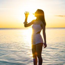 MANEE Group Mateusz Zacharow - Sylwetka kobiety pijącej napój z butelki na tle zachodzącego słońca nad morzem, woda odbija promienie słoneczne.