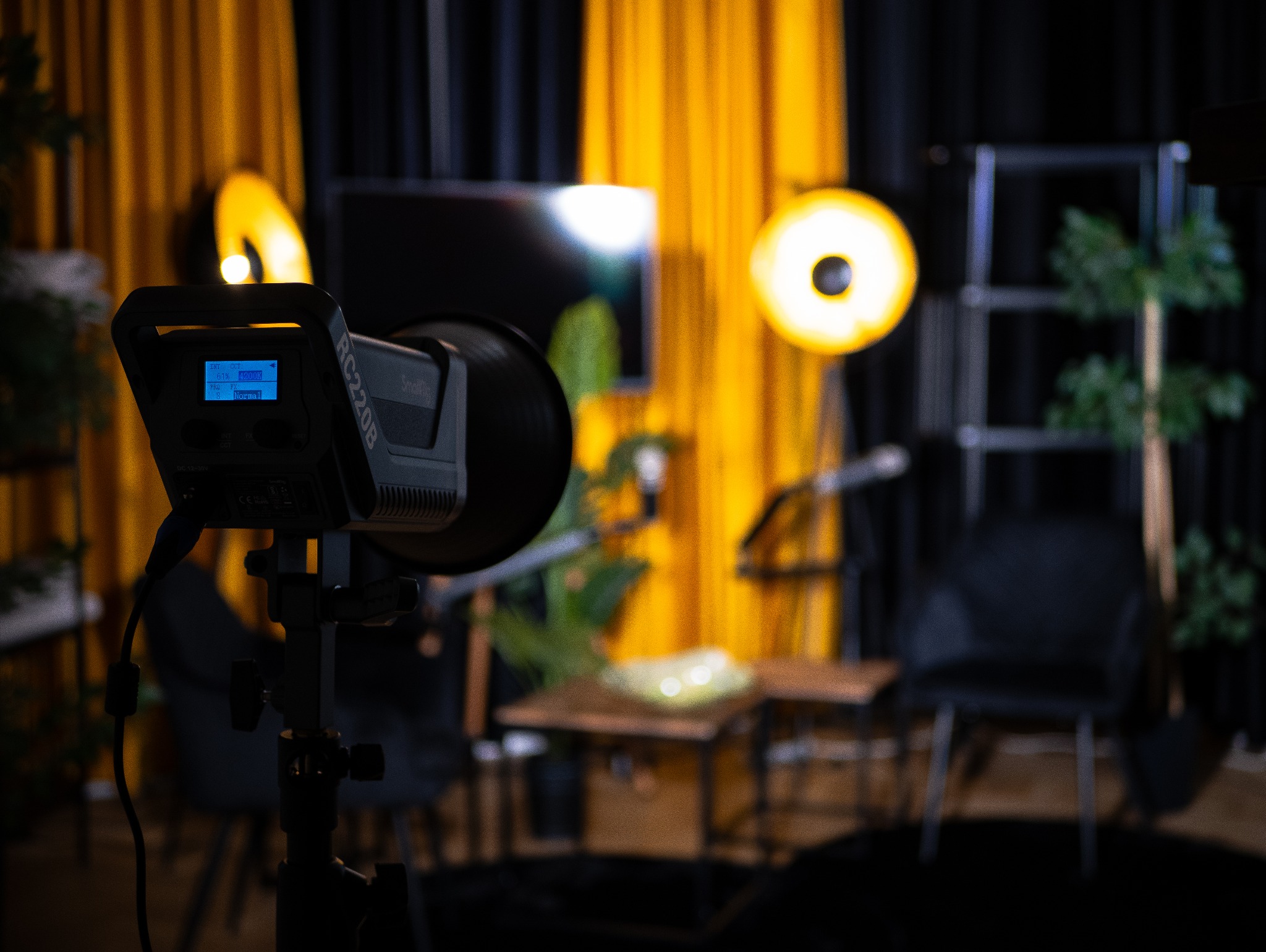 Profesjonalne oświetlenie studyjne SmallRig RC220B na statywie, z widocznym ekranem LCD, ustawione w studio z żółtymi i czarnymi zasłonami w tle, dodatkowymi lampami pierścieniowymi i elementami...