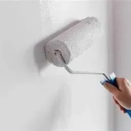 Świeżo pomalowana, biała ściana z widocznym śladem mokrej farby i wałkiem w dłoni podczas aplikacji.