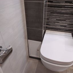 Instalpos - Ściana w łazience z różnymi rodzajami płytek: białe, szare i mozaika, obok podwieszana toaleta i rewizja.