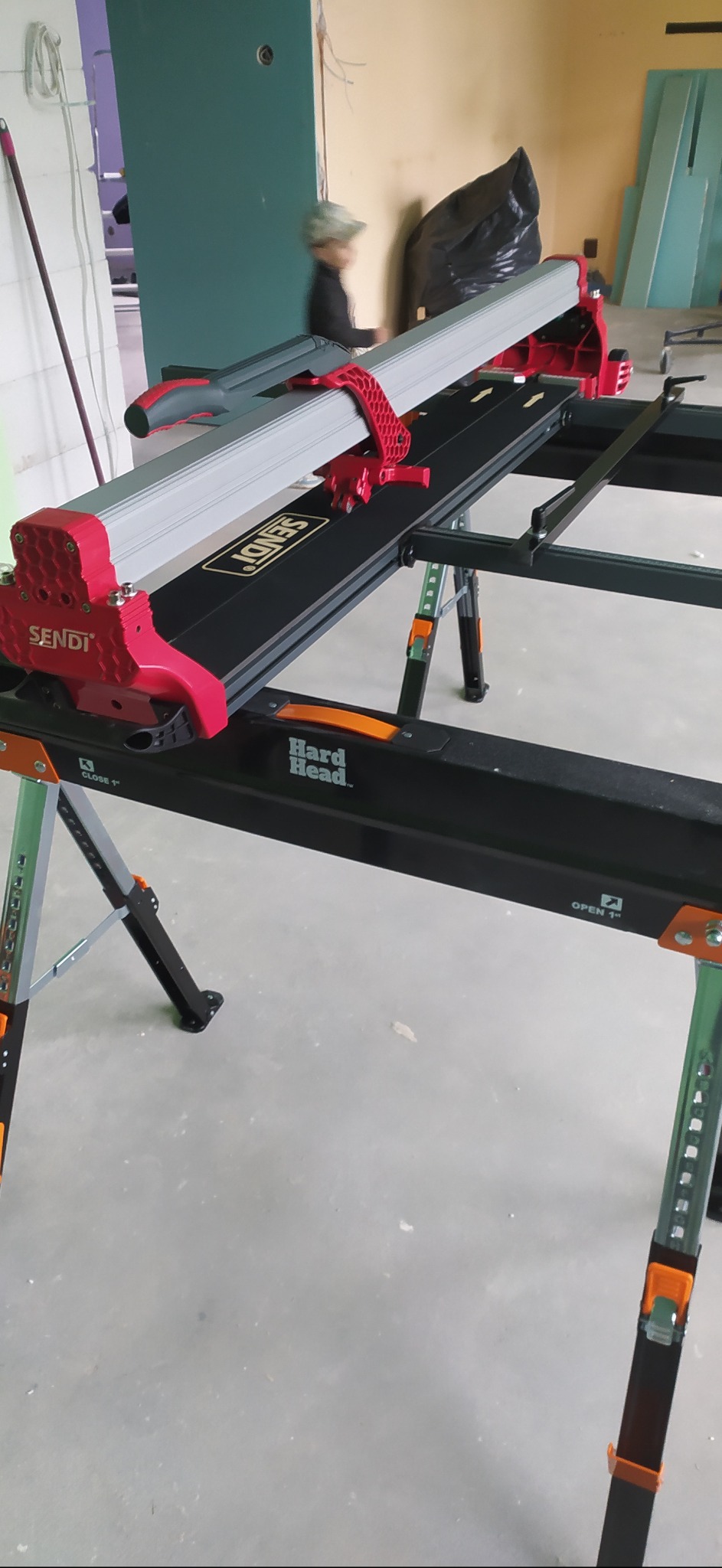 Profesjonalna przecinarka do płytek ceramicznych marki Sendi na regulowanym stole roboczym Hard Head, gotowa do użycia w pomieszczeniu w trakcie remontu.
