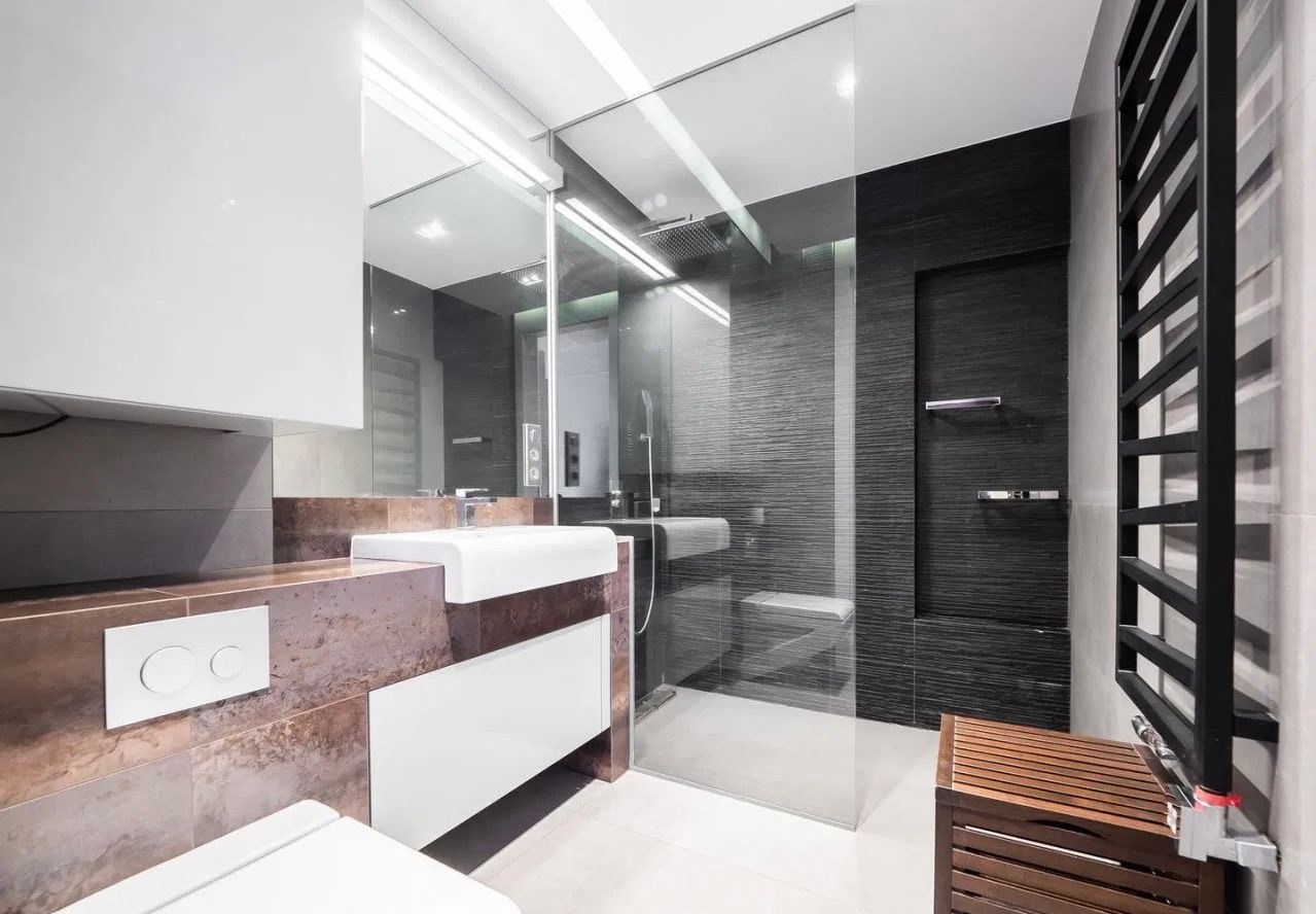 Nowoczesna łazienka z kabiną prysznicową typu walk-in, umywalką nablatową na blacie z efektem rdzy i czarnym grzejnikiem drabinkowym.