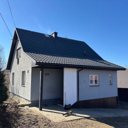 DECKER Paweł Mól - Nowoczesny dom jednorodzinny z ciemnoszarą dachówką, numerem 595 nad wjazdem i dmuchawą do liści na kostce brukowej przed wjazdem.