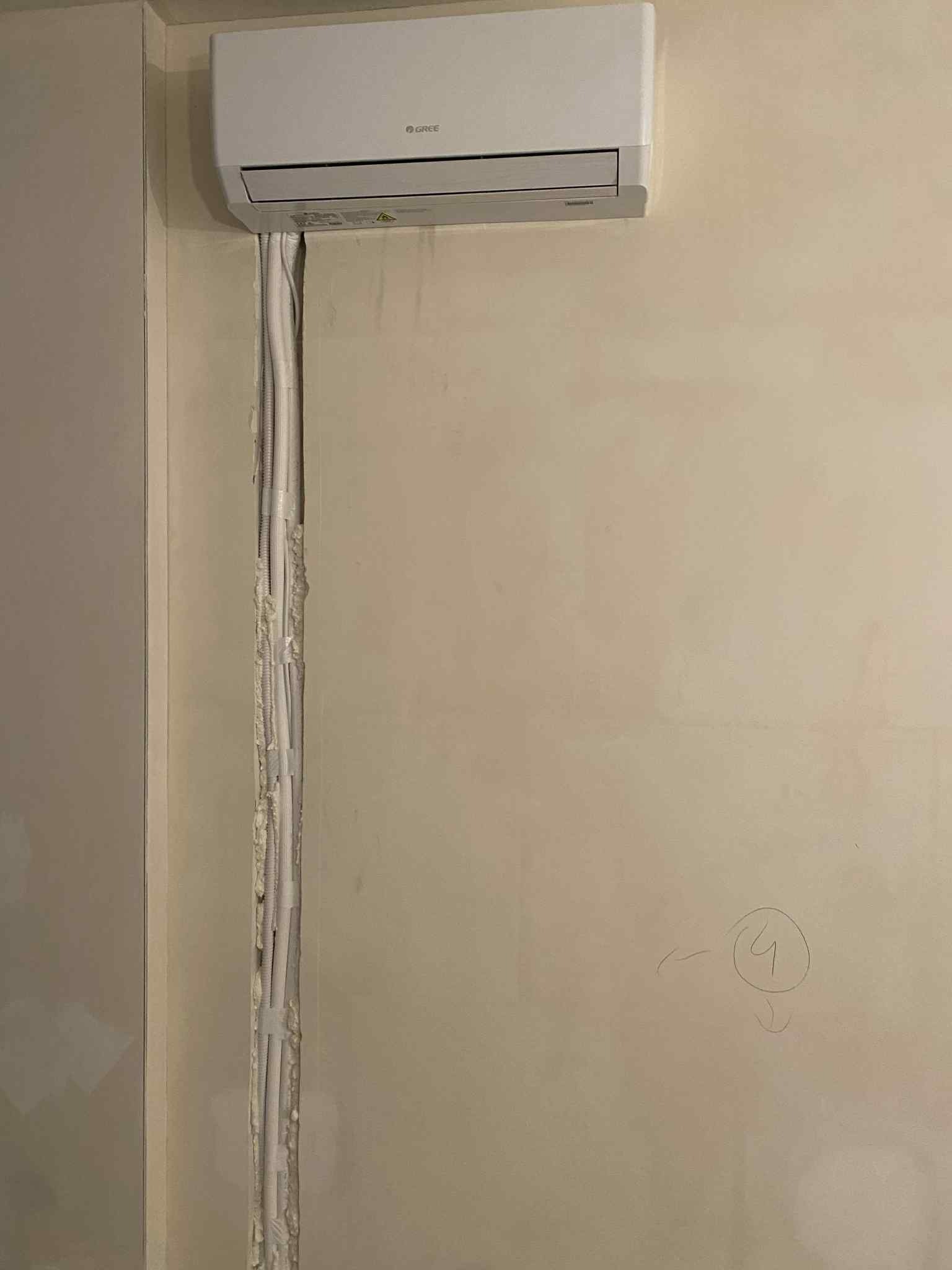 Biały klimatyzator na ścianie z widocznymi przewodami w bruździe, przygotowanymi do zakrycia. Widoczne ślady po montażu.