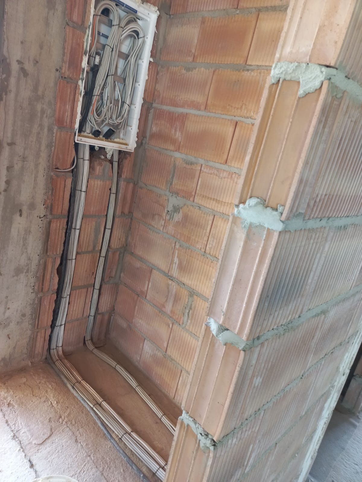 Wewnętrzna instalacja przewodów elektrycznych w ścianie z cegły, widoczna puszka rozdzielcza z okablowaniem.
