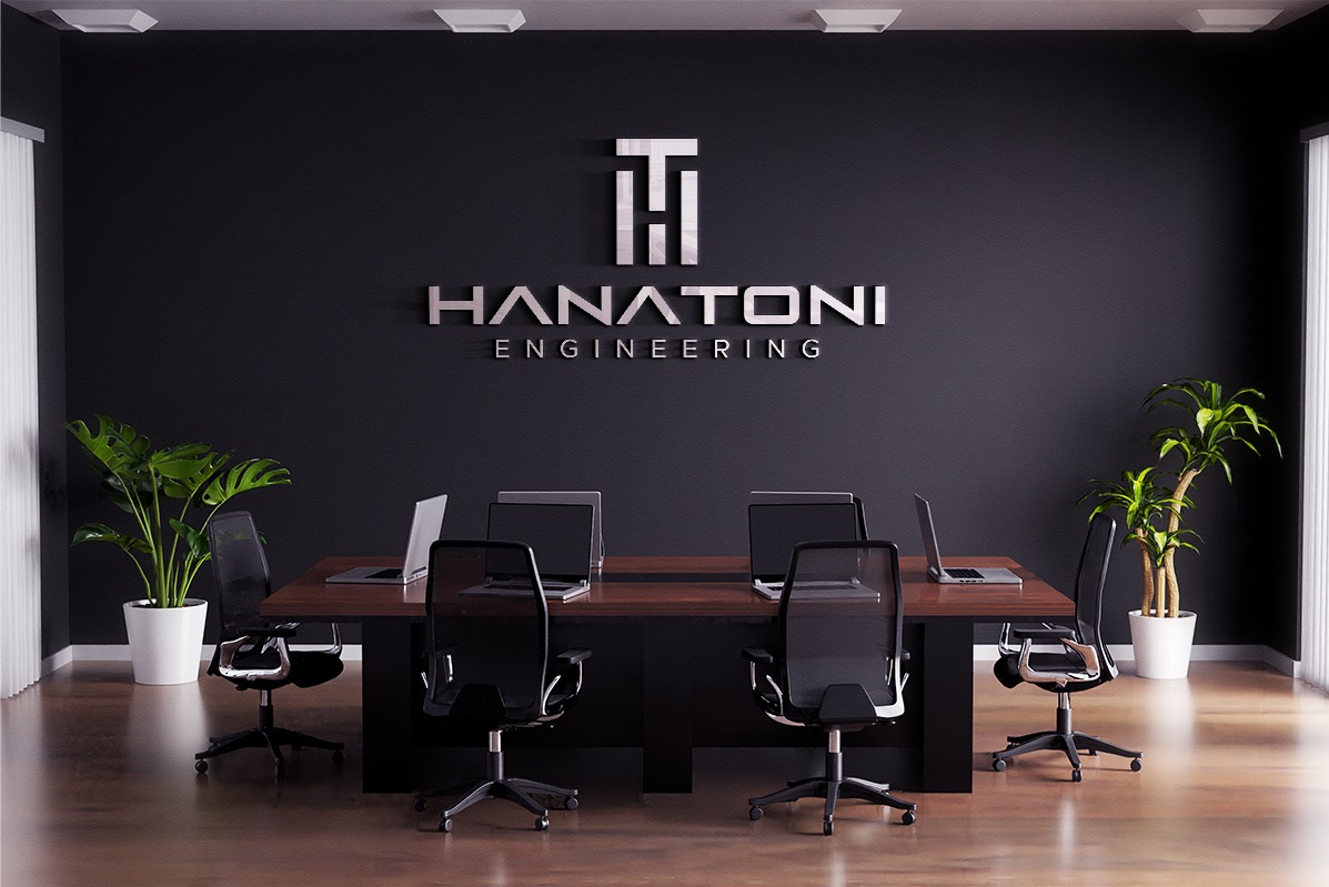 Wizualizacja biura z ciemną ścianą, na której umieszczono srebrne logo 'HANATONI ENGINEERING'. Na drewnianym stole stoją laptopy, a wokół niego znajdują się czarne krzesła biurowe. Dwie rośliny...