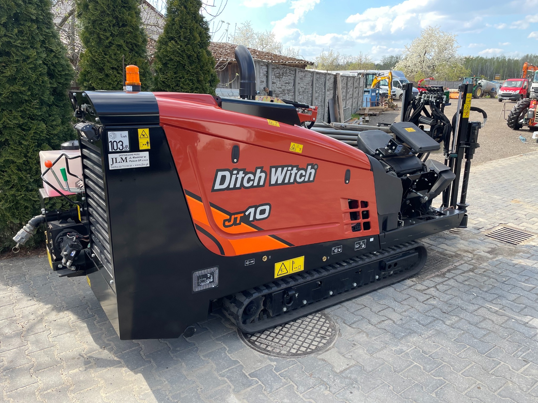 Pomarańczowo-czarna maszyna Ditch Witch JT10 do prac ziemnych, stojąca na kostce brukowej, z widocznymi detalami jak gąsienice, panel sterowania i logo firmy.