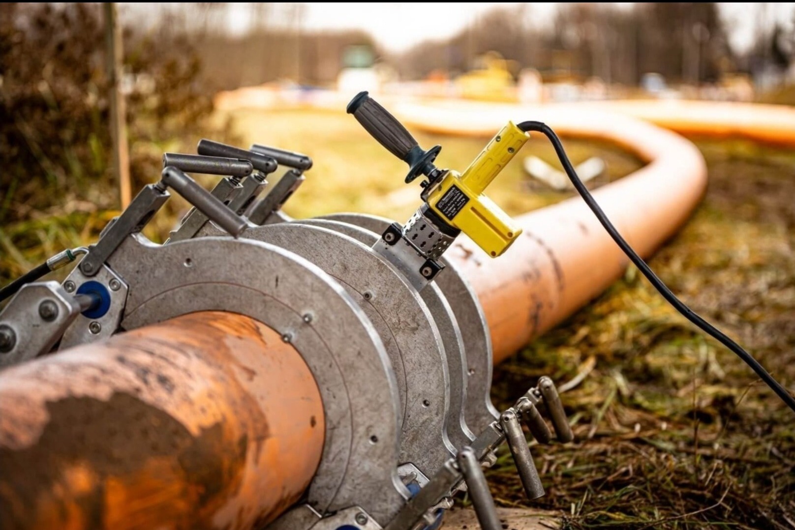 Zgrzewarka doczołowa do rur z tworzyw sztucznych, widoczna w trakcie pracy na zewnątrz, rura lekko zabrudzona ziemią.
