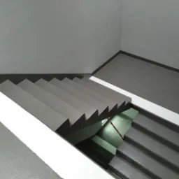 Klatka schodowa z szarymi schodami i białymi pasami na ścianach, widok z góry na dół.