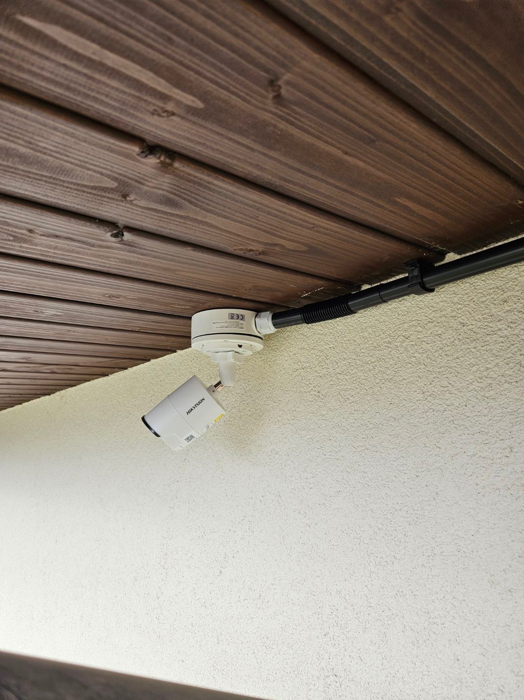 Kamera przemysłowa Hikvision zamontowana pod drewnianym sufitem, przewody zabezpieczone peszlem.