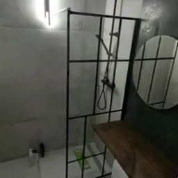 Nowoczesna łazienka z kabiną prysznicową w stylu loft, czarną armaturą, okrągłym lustrem i blatem z drewna nad pralką.