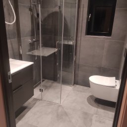 Remonty Łazieki - Nowoczesna łazienka w szarościach: kabina prysznicowa ze szkła, podwieszana toaleta i umywalka z szafką. Minimalistyczny design, ciemna rama okna.
