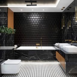 Biały Kruk - Elegancka łazienka z czarnymi płytkami metra, marmurowymi ścianami i podłogą w biało-czarną mozaikę, złota armatura, dwie białe umywalki i wisząca toaleta.