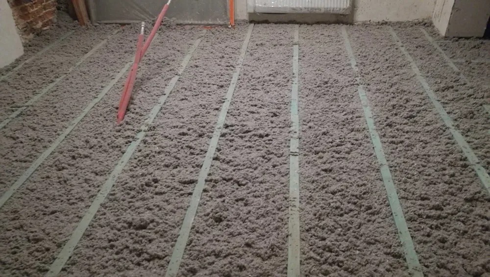 Podłoga pokryta warstwą izolacyjną z wełny mineralnej, widoczne listwy dystansowe, przygotowanie do dalszych prac wykończeniowych.