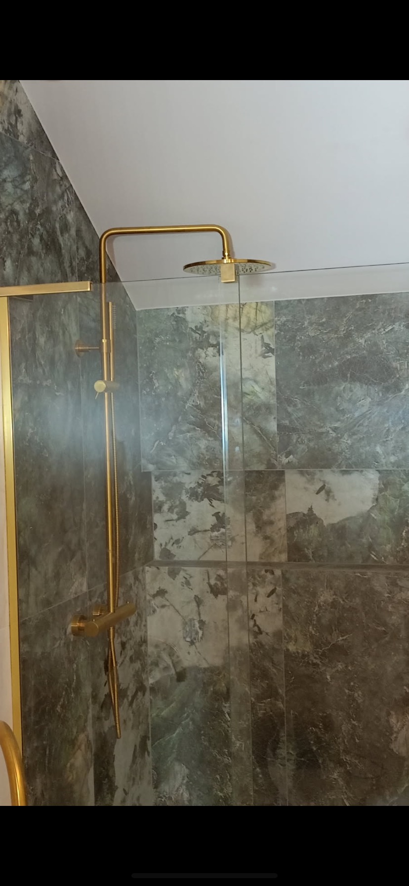 Złota armatura w kabinie prysznicowej z szarymi płytkami imitującymi marmur.