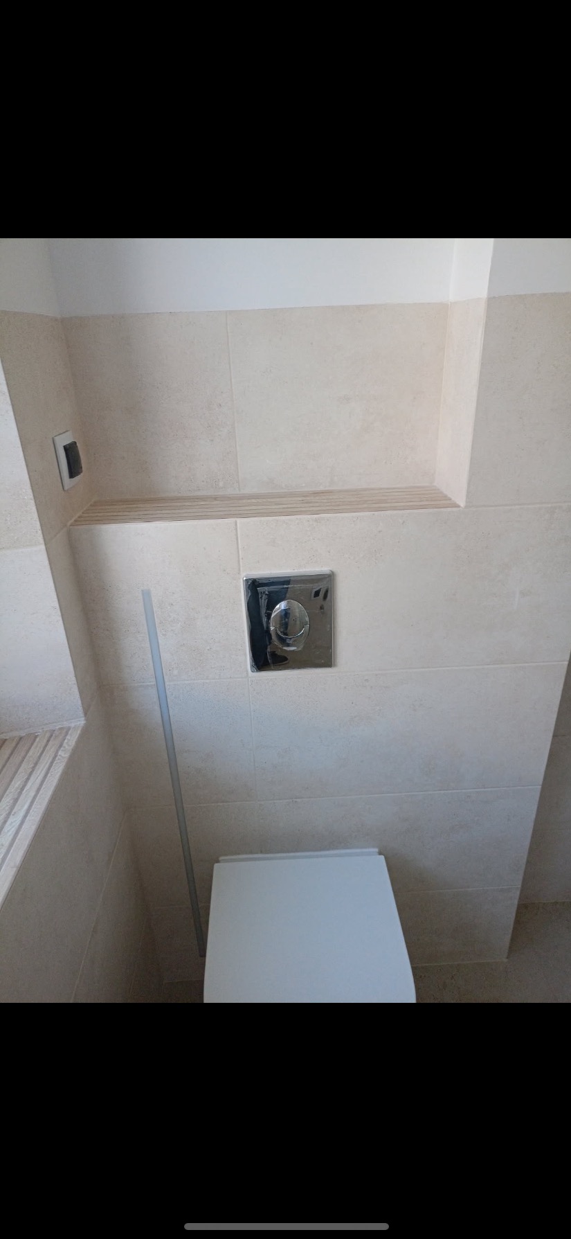 Nowoczesna toaleta podtynkowa z chromowanym przyciskiem spłukującym, obudowana beżowymi płytkami ceramicznymi z wnęką