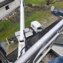 WEZA Mirosław Sitko - Widok z góry na podnośnik koszowy ustawiony obok budynku mieszkalnego, z widocznym fragmentem dachu, ogrodu i białej ciężarówki na posesji.