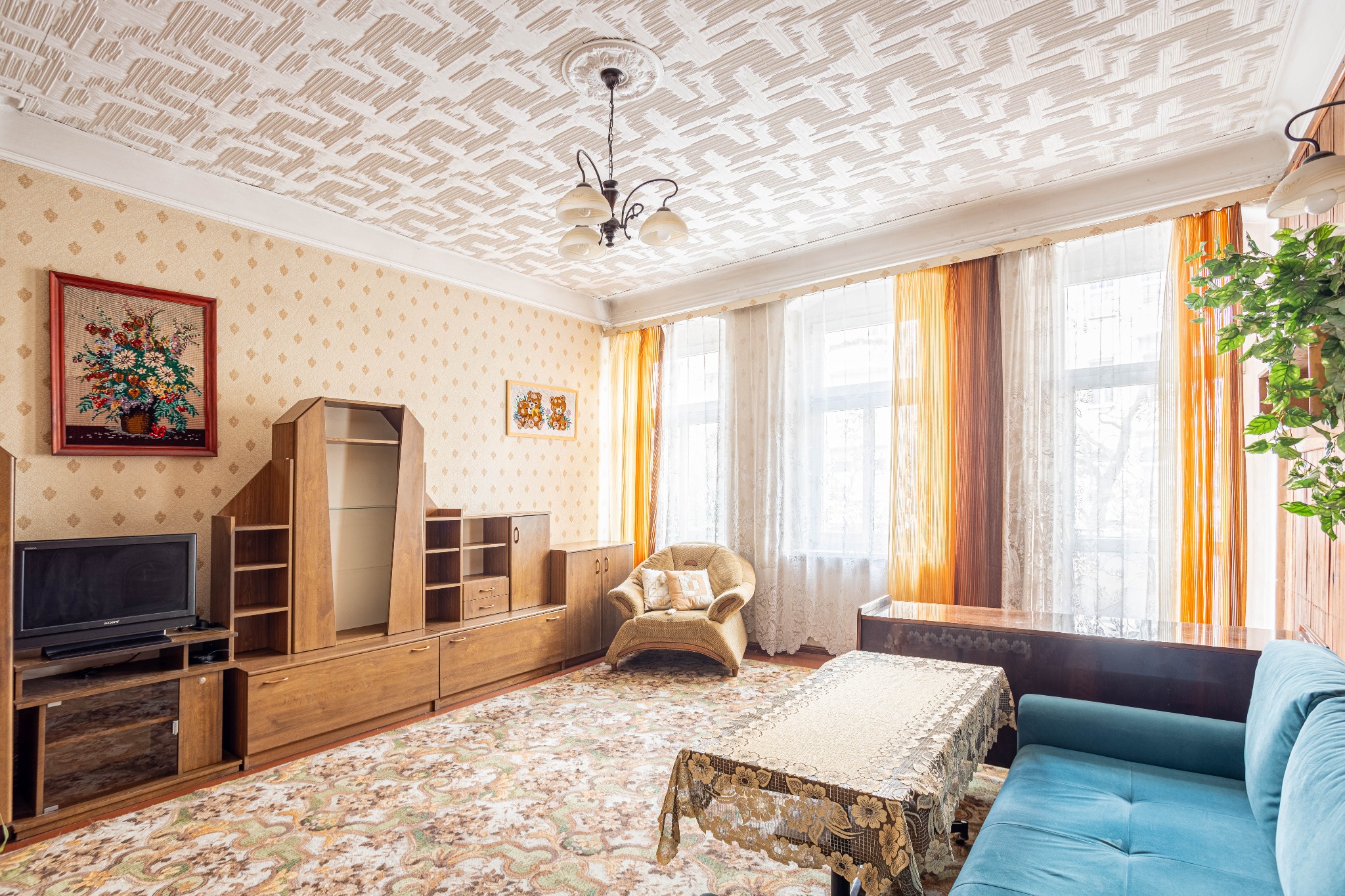 Pokój dzienny z meblami z lat 80., wzorzysta tapeta i sufit, telewizor Sony i niebieska kanapa.