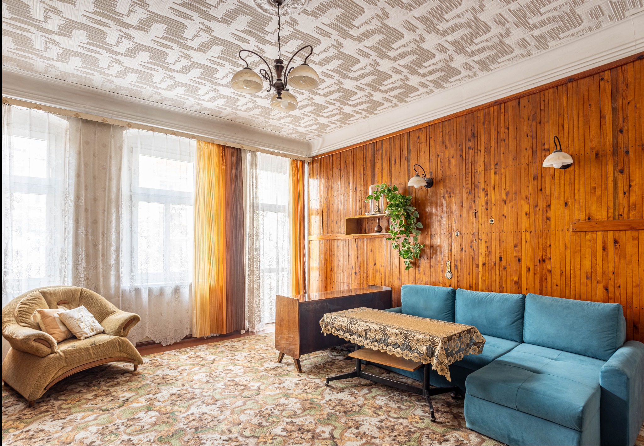 Pokój dzienny z drewnianą boazerią, turkusową sofą, wzorzystym dywanem i lampą wiszącą, styl retro.