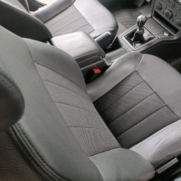 Szaleniec Detailingu konin - Wnętrze samochodu z widocznymi szarymi skórzanymi fotelami z materiałowymi wstawkami, konsola środkowa z dźwignią zmiany biegów i elementami sterowania, uchwycone z bliska.