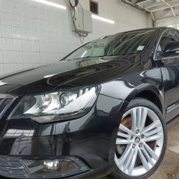 Szaleniec Detailingu konin - Błyszczący, czarny samochód Skoda Superb po umyciu, widoczny z bliska, z detalami felg i reflektorów.