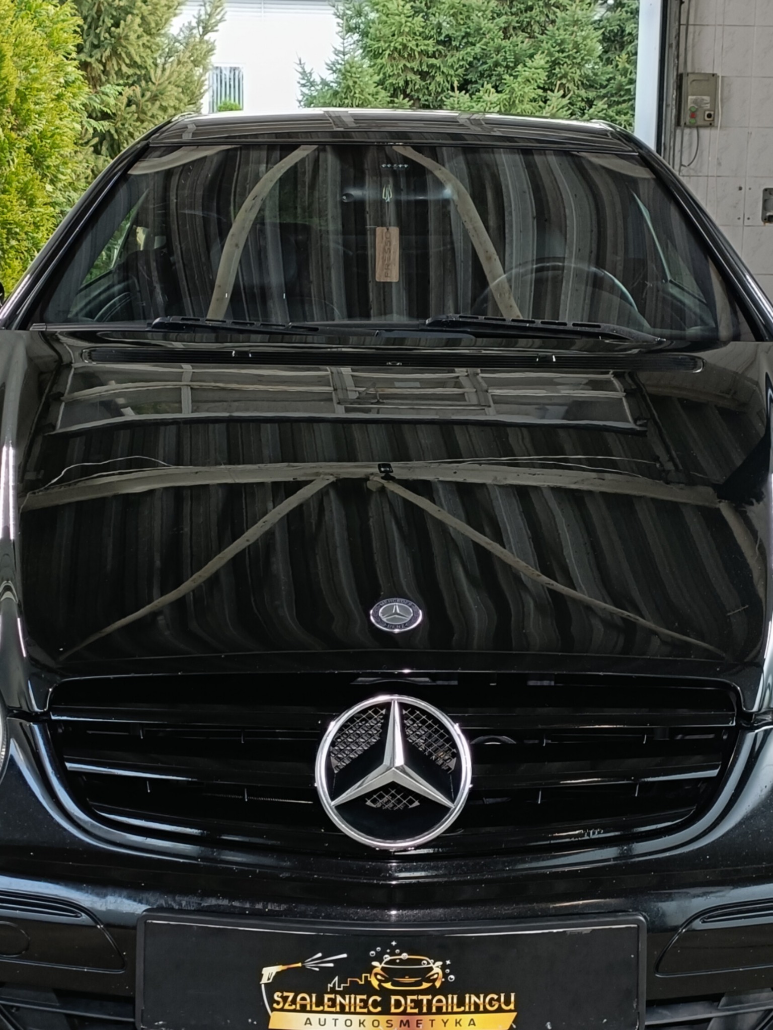 Błyszczący, czarny Mercedes CLK 320 Avantgarde po dwuetapowej korekcie lakieru, widok na maskę i grill z logo firmy detailingowej w dolnej części kadru.