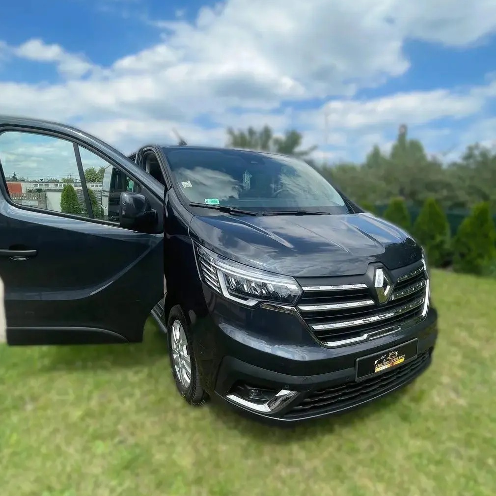 Czarny van Renault Trafic z otwartymi drzwiami przesuwnymi na trawniku, widoczne logo firmy na przednim zderzaku.