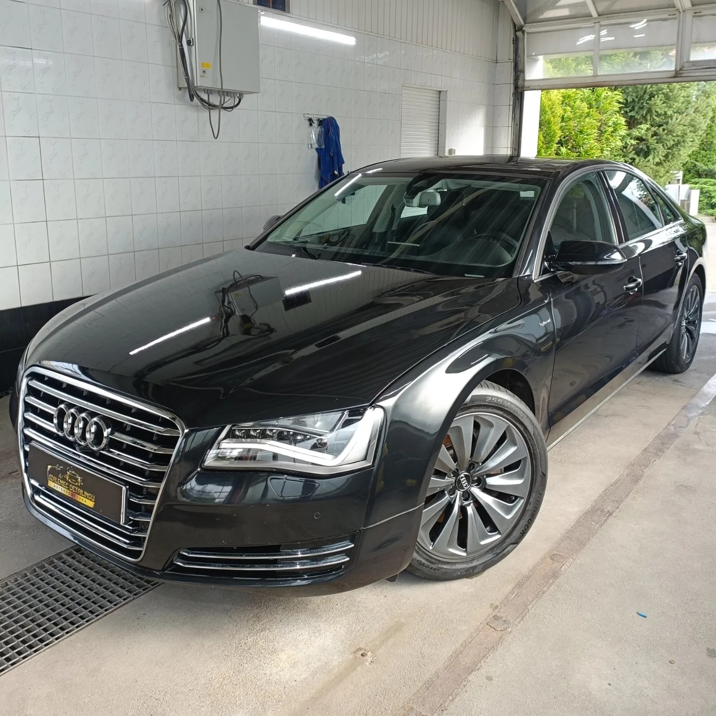 Błyszczący czarny Audi A8 po detailingu, zaparkowany w jasnym pomieszczeniu z wyłożonymi kafelkami ścianami i kratką ściekową w podłodze.