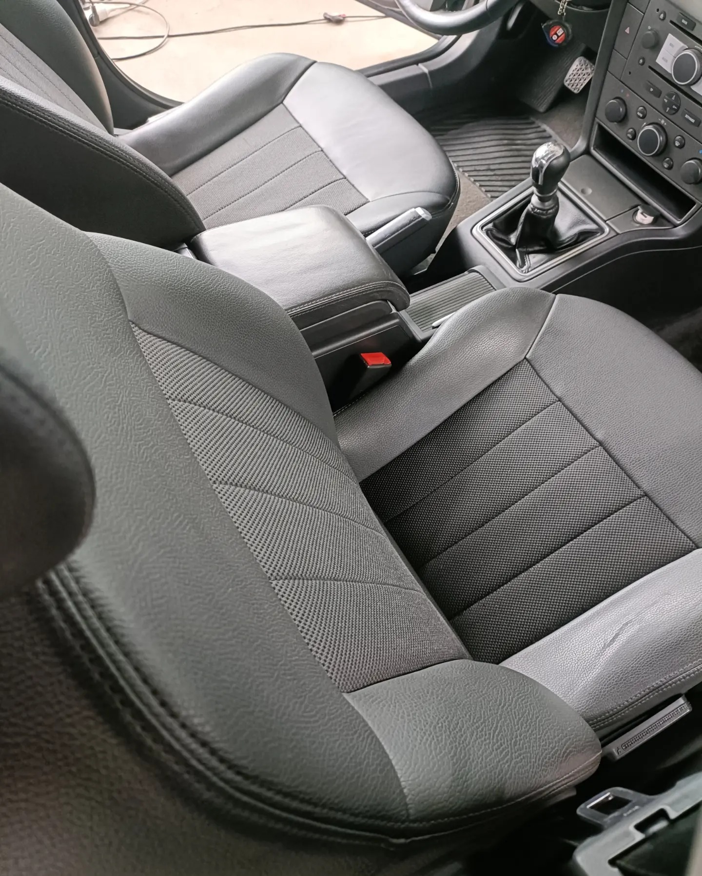 Wnętrze samochodu z widocznymi szarymi skórzanymi fotelami z materiałowymi wstawkami, konsola środkowa z dźwignią zmiany biegów i elementami sterowania, uchwycone z bliska.