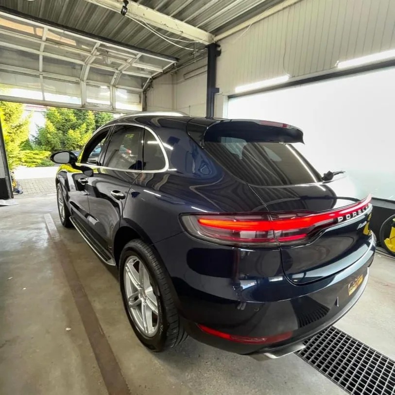 Błyszczący, granatowy samochód Porsche Macan po kompleksowym czyszczeniu, widoczny w jasnym pomieszczeniu z otwartą bramą garażową i zielenią na zewnątrz.