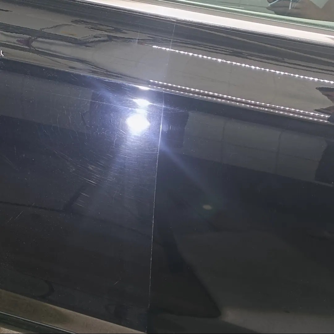 Fragment czarnej, błyszczącej powierzchni z widocznymi rysami i hologramami przed polerowaniem, oświetlony punktowym światłem inspekcyjnym.