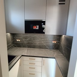 POLI IMAGER - Nowoczesna kuchnia z szarymi szafkami górnymi, blatem imitującym marmur i białymi szafkami dolnymi z złotymi uchwytami. Widoczne gniazdka i wbudowana mikrofalówka.