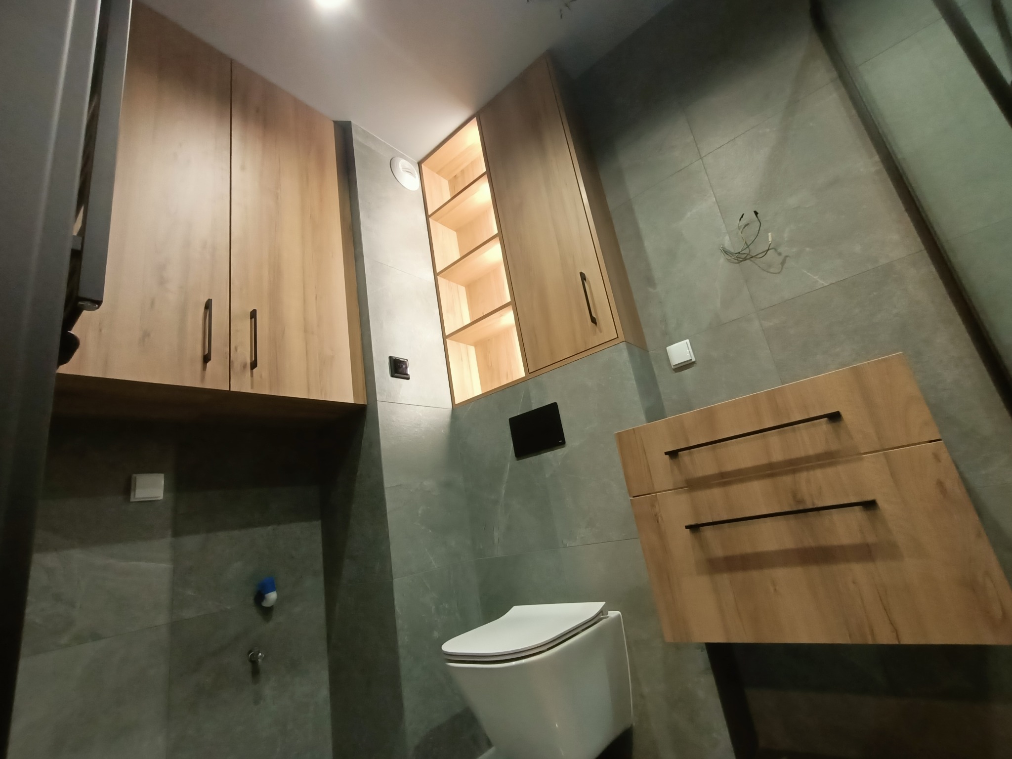 Nowoczesna łazienka z drewnianymi szafkami na wymiar, szarą glazurą i podświetlaną półką w Libertowie. Minimalistyczny design i funkcjonalne rozwiązania.