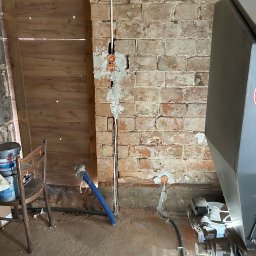 Dawid Piskorz Usługi Elektryczne - Instalacja elektryczna w trakcie prac: przewody w bruzdach, puszki podtynkowe w surowej ceglanej ścianie. Widoczne narzędzia i materiały budowlane.