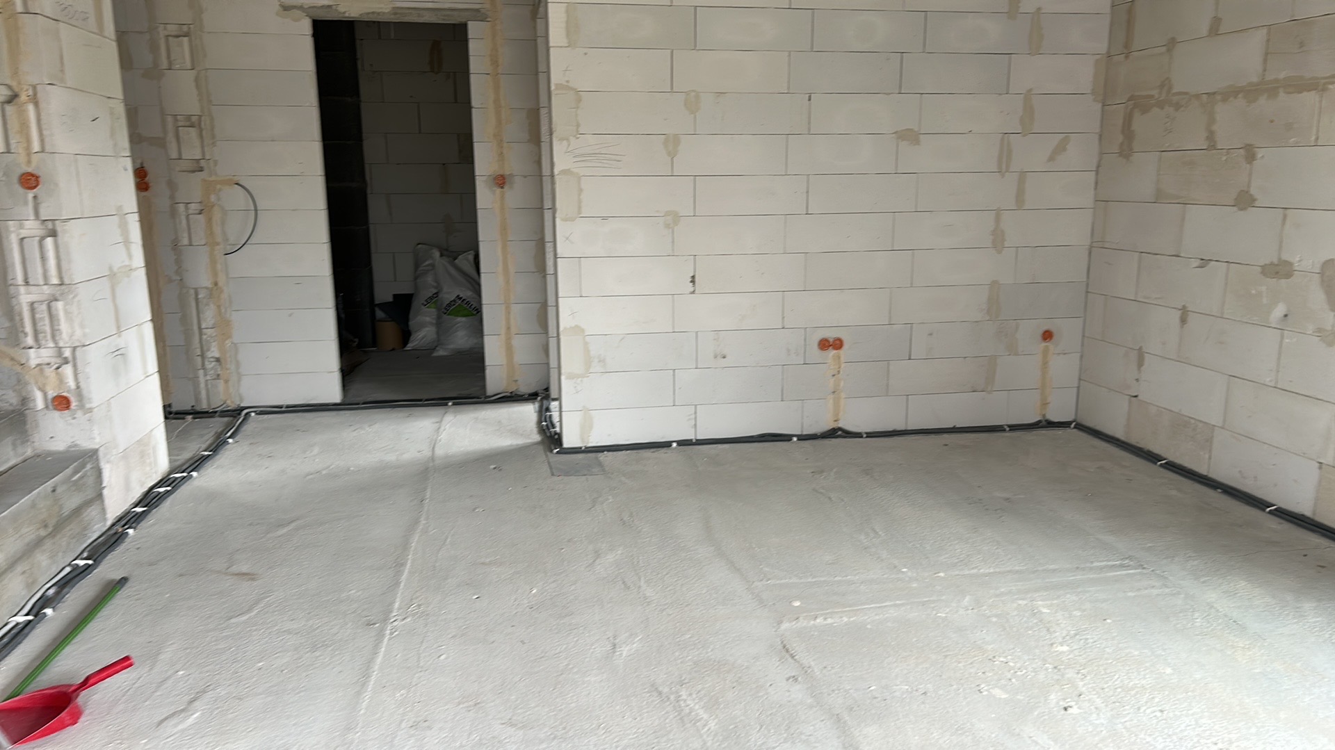 Surowy stan wnętrza z widoczną instalacją elektryczną w listwach przypodłogowych i puszkami w ścianach z betonu komórkowego. Na podłodze widoczne narzędzia.