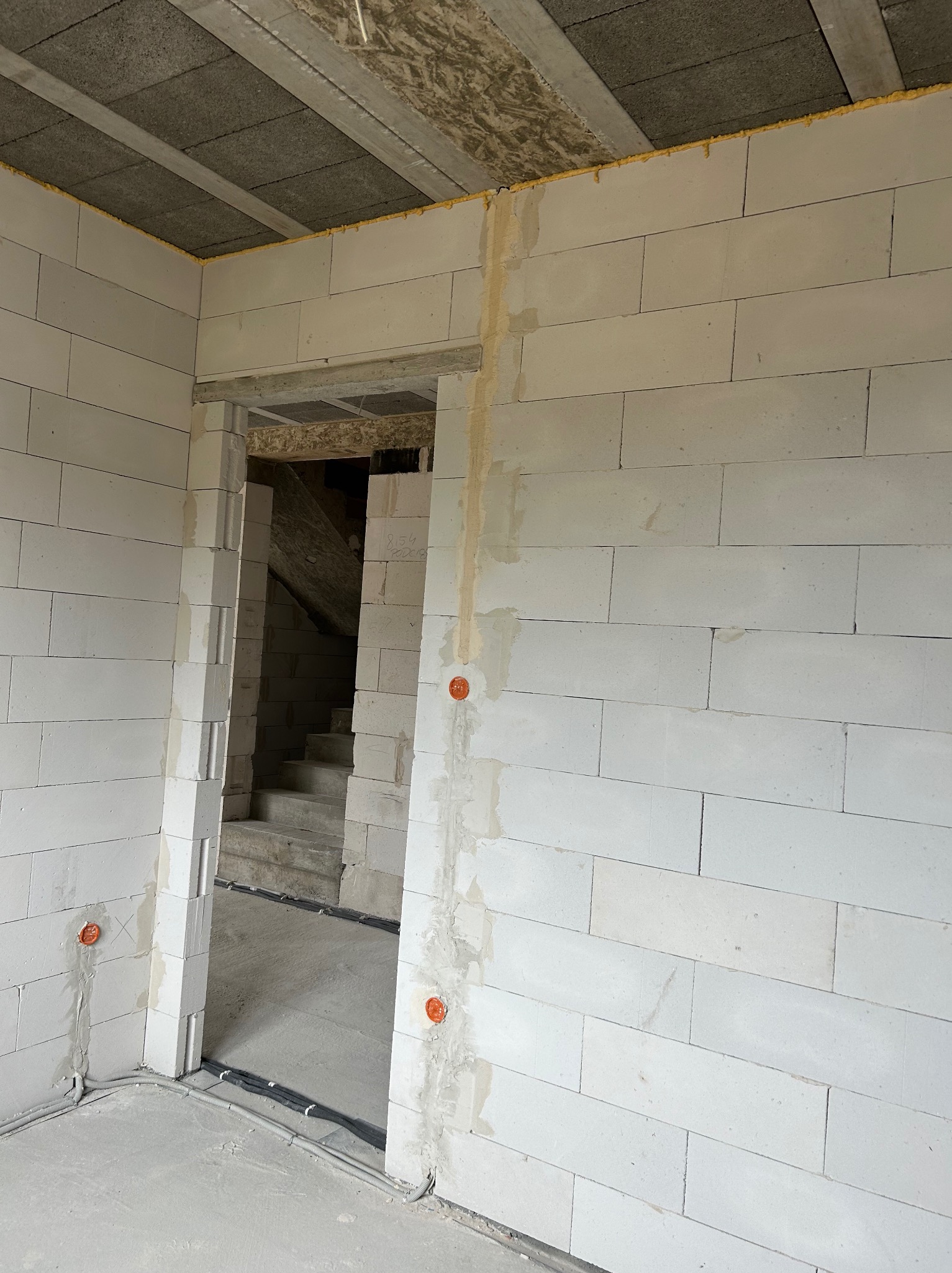 Wnętrze w stanie surowym z widocznymi przewodami elektrycznymi w peszlach ułożonymi wzdłuż ściany oraz puszkami instalacyjnymi w ścianie z betonu komórkowego.