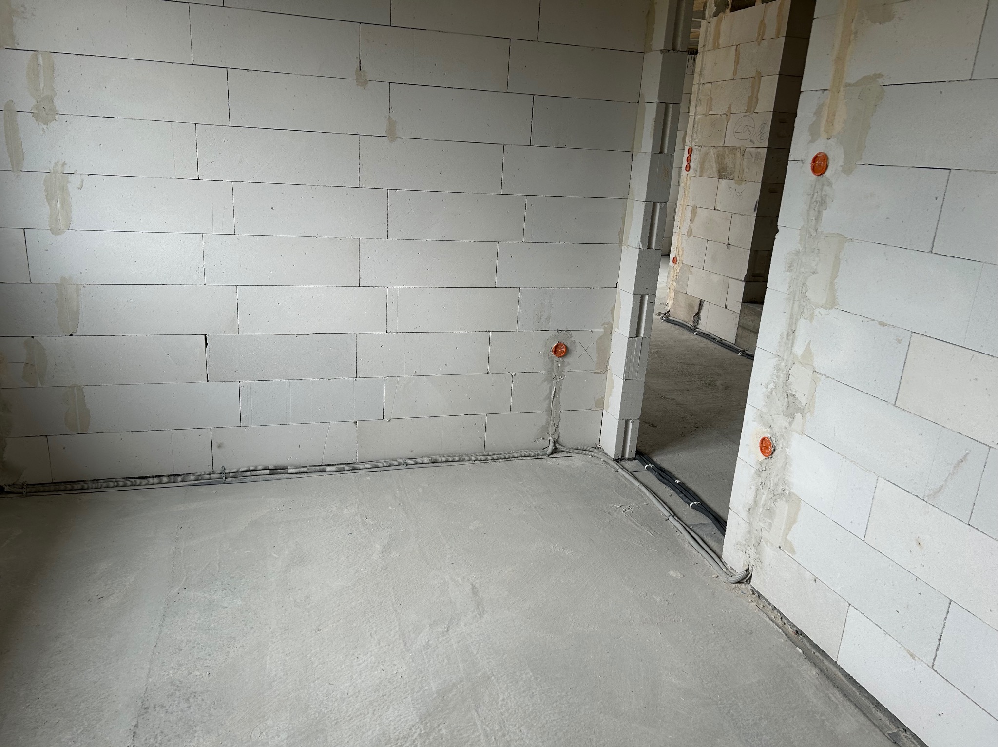 Surowy stan: ściany z betonu komórkowego z puszkami elektrycznymi i przewodami w peszlach na podłodze, gotowe do dalszych prac instalacyjnych.