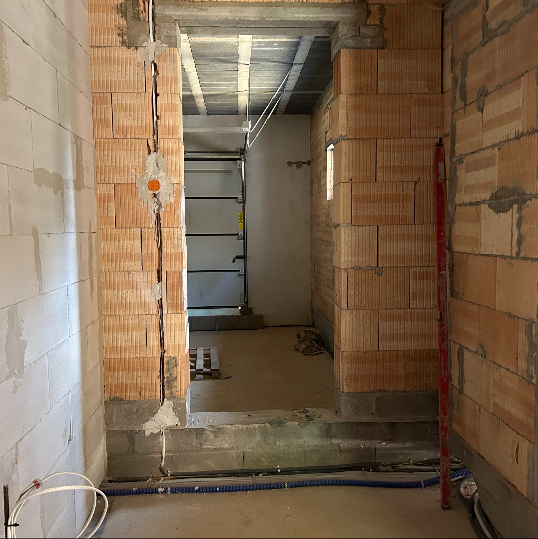Wnętrze w trakcie budowy. Widoczne kable elektryczne w ścianie z cegły, puszka instalacyjna, peszle pod podłogą, surowy stan wykończenia.