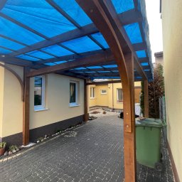 Tomek Cholewinski - Drewniana konstrukcja z niebieskim zadaszeniem, prawdopodobnie w trakcie budowy w Końskich, z widocznym koszem na śmieci i kostką brukową.