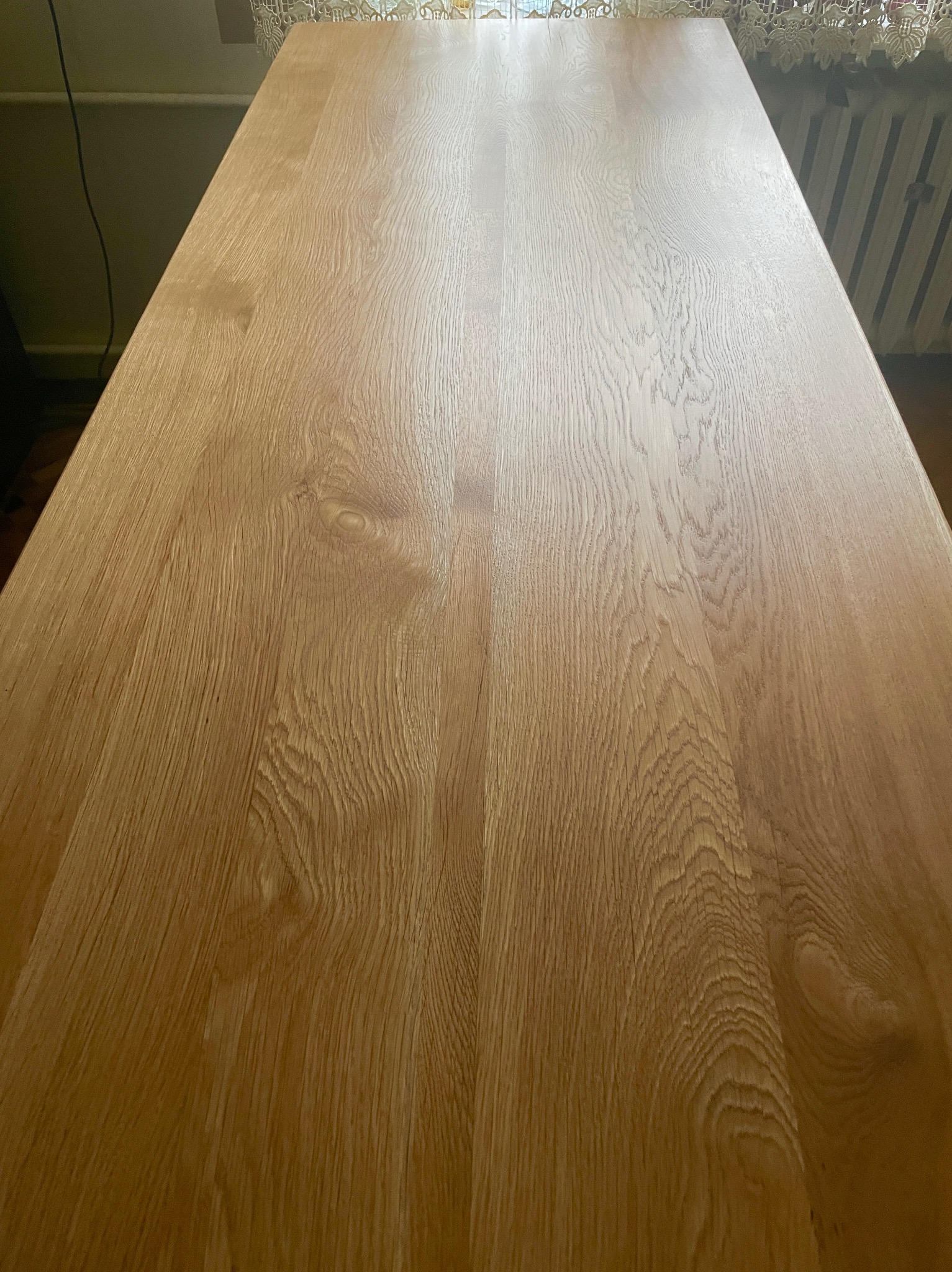 Jasna, lakierowana powierzchnia drewniana z wyraźnym usłojeniem, prawdopodobnie blat stołu lub element schodów, sfotografowana pod kątem z góry.