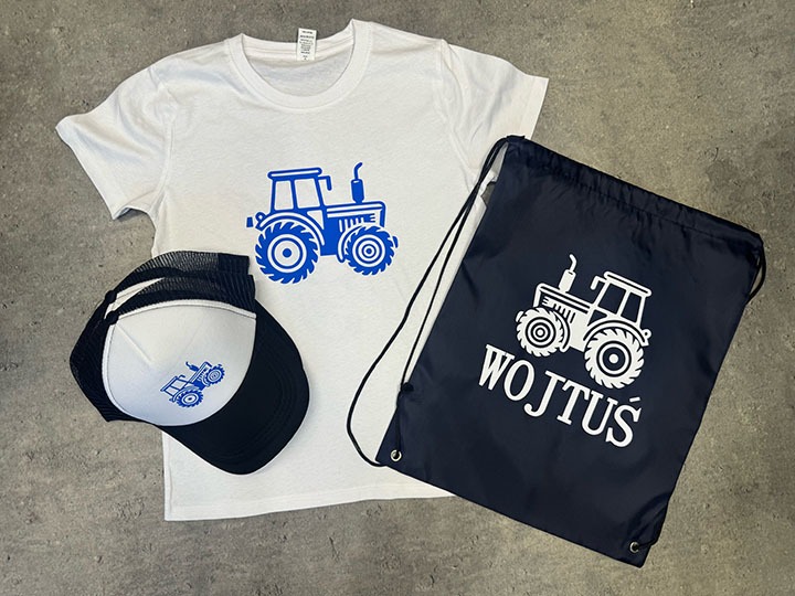 Biała koszulka, czarno-biała czapka z daszkiem i granatowy worek ze sznurkiem, wszystkie z nadrukiem niebieskiego/białego traktora, worek dodatkowo z napisem 'WOJTUŚ'.
