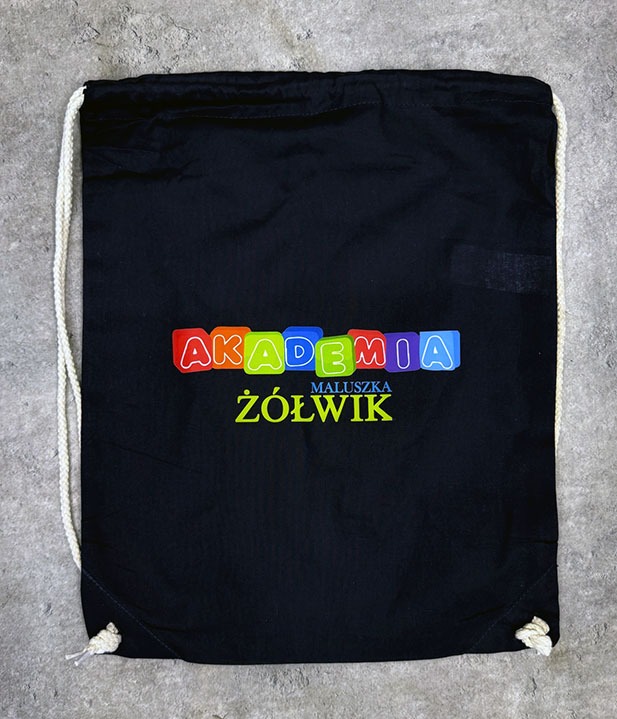 Czarny worek gimnastyczny ze sznurkami, z kolorowym nadrukiem 'AKADEMIA MALUSZKA ŻÓŁWIK' na szarym tle.