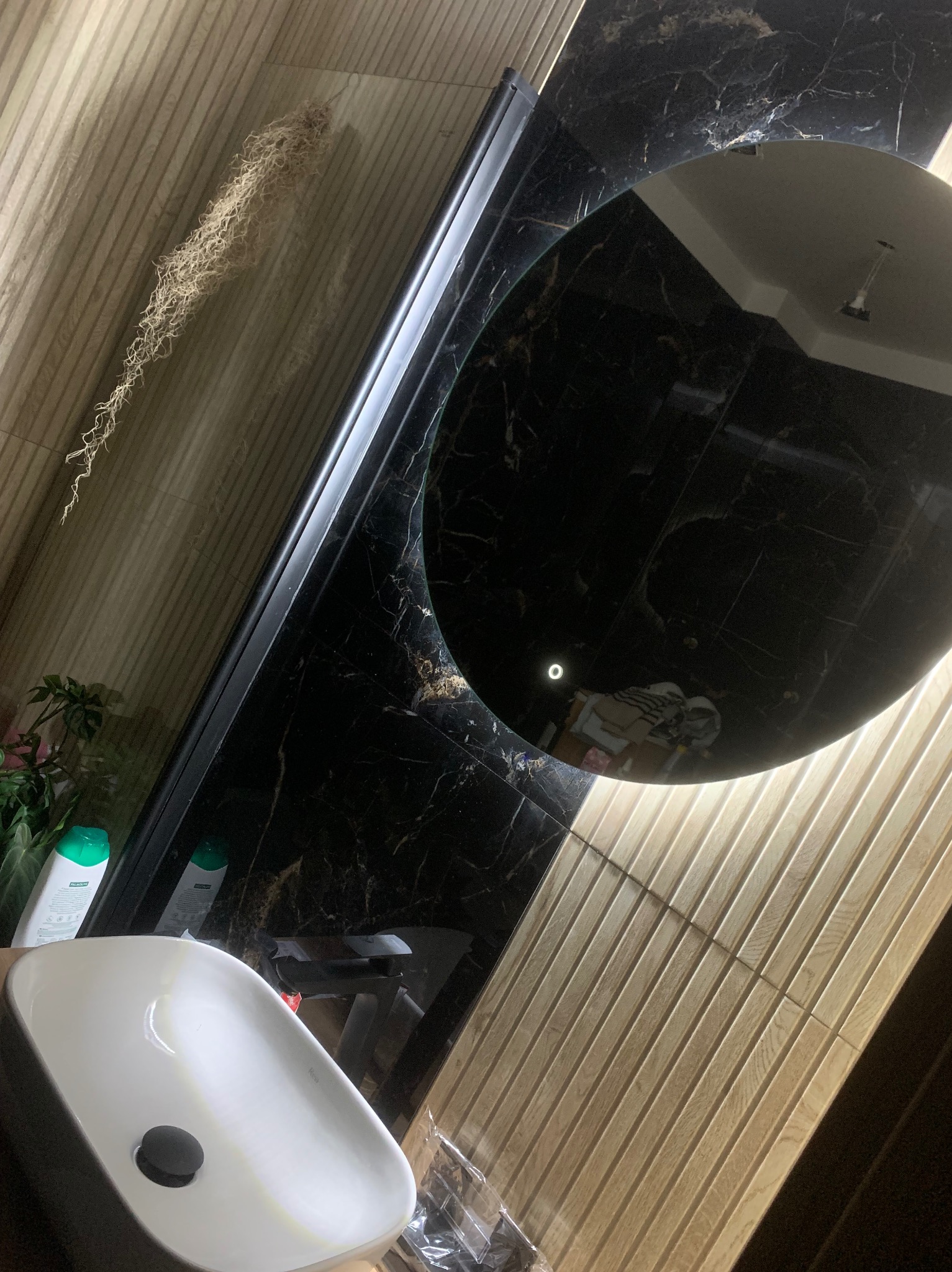 Umywalka nablatowa REA w łazience z czarnym marmurem i drewnopodobnymi płytkami ściennymi, okrągłe podświetlane lustro odbija sufit.