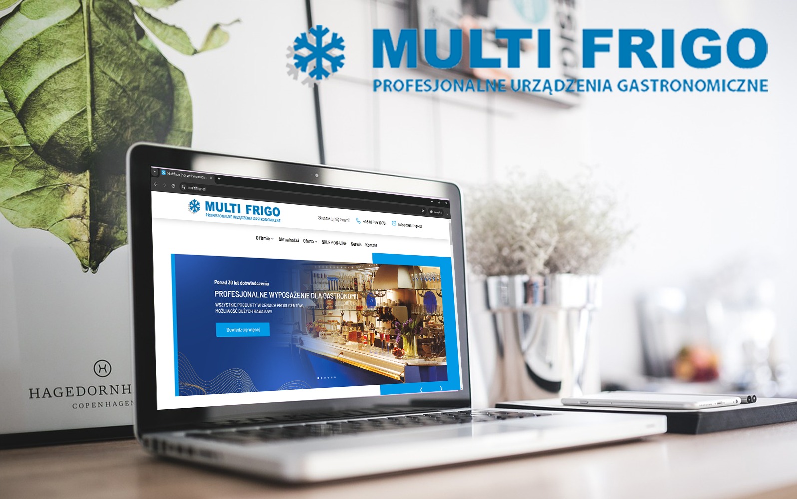 Laptop wyświetlający stronę internetową Multi Frigo z ofertą profesjonalnych urządzeń gastronomicznych, obok notatnik i smartfon, w tle dekoracje roślinne.