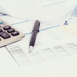 TAXNORD Biuro Rachunkowe - Kalkulator, długopis i banknoty euro na tle arkusza kalkulacyjnego z danymi liczbowymi.