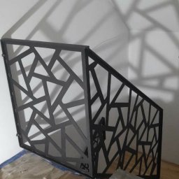 TRÓJSPAW - Czarna, metalowa balustrada schodowa o geometrycznym wzorze, w trakcie montażu, zabezpieczona folią podłoga, widoczne narzędzia.