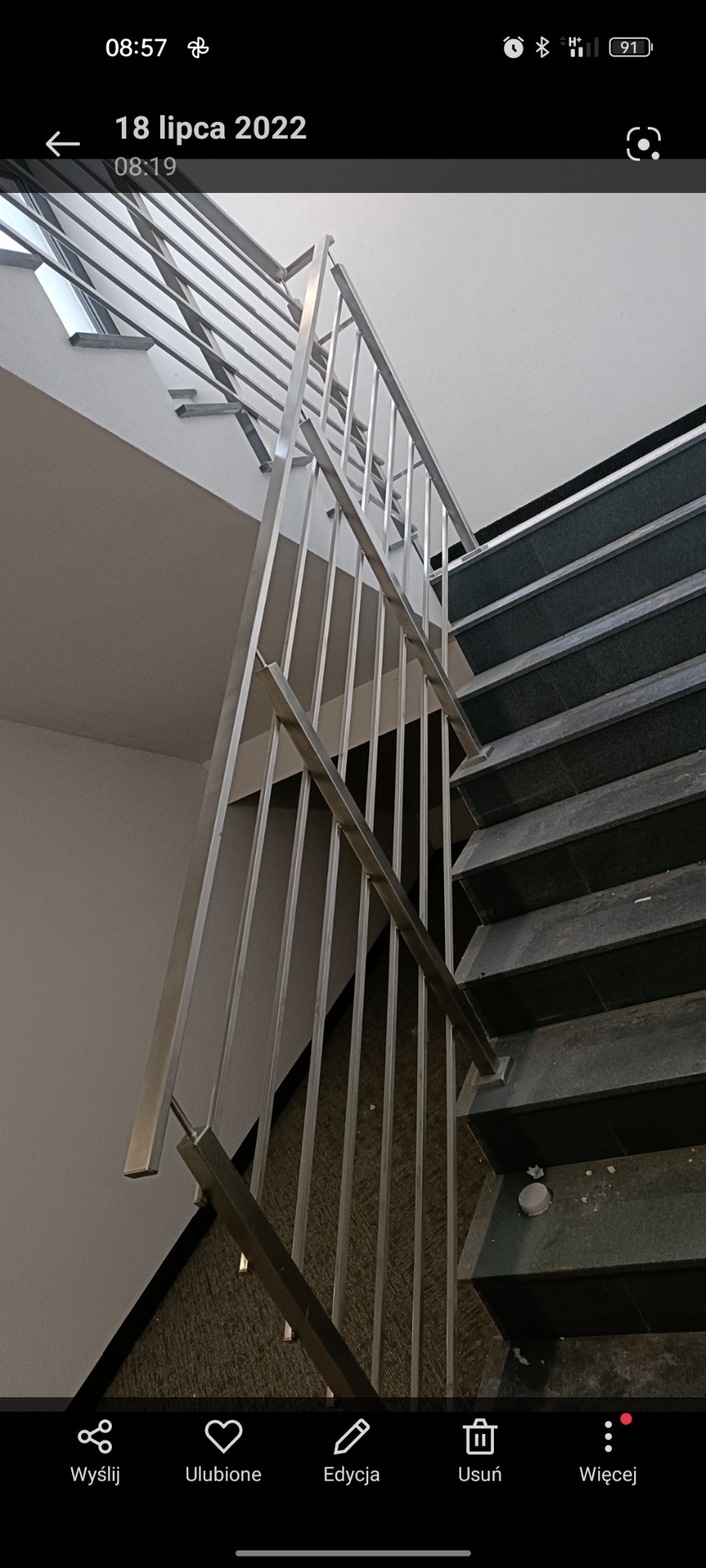 Wewnętrzne schody z ciemnego kamienia z nowoczesną, minimalistyczną balustradą ze stali nierdzewnej, widok z dołu, oświetlenie górne.