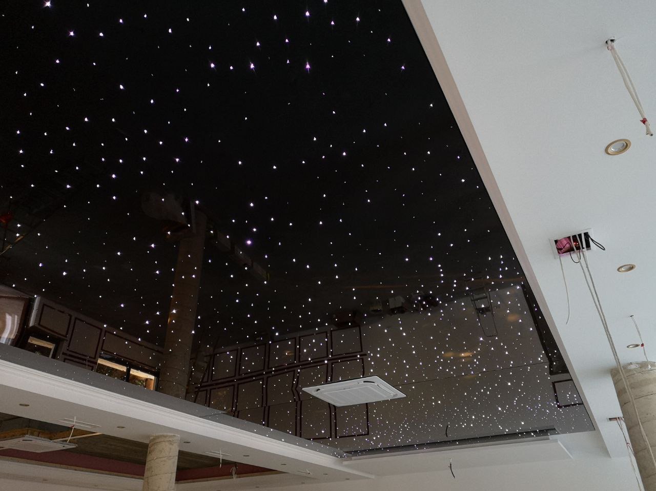 Czarny błyszczący sufit z punktowym oświetleniem imitującym gwiazdy, widoczny fragment instalacji elektrycznej oraz kratka wentylacyjna.